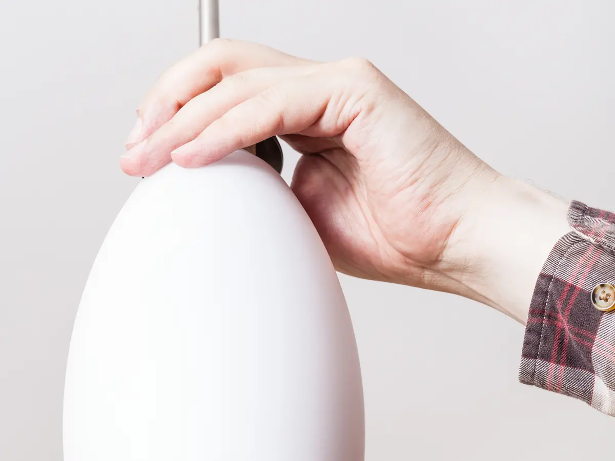 A hand fitting a white glass pendant shade to a ceiling flex.