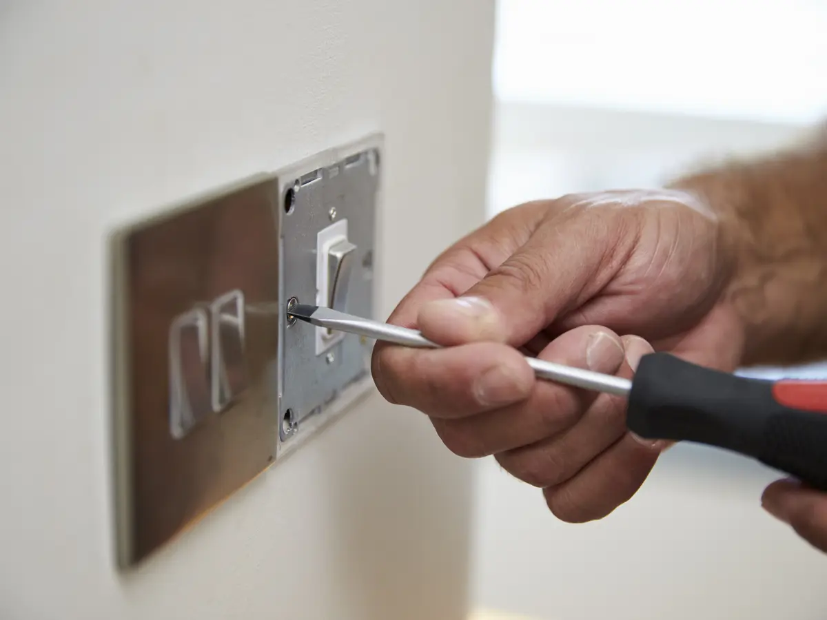 A screwdriver fixing a brushed steel double light switch plate back onto its box.