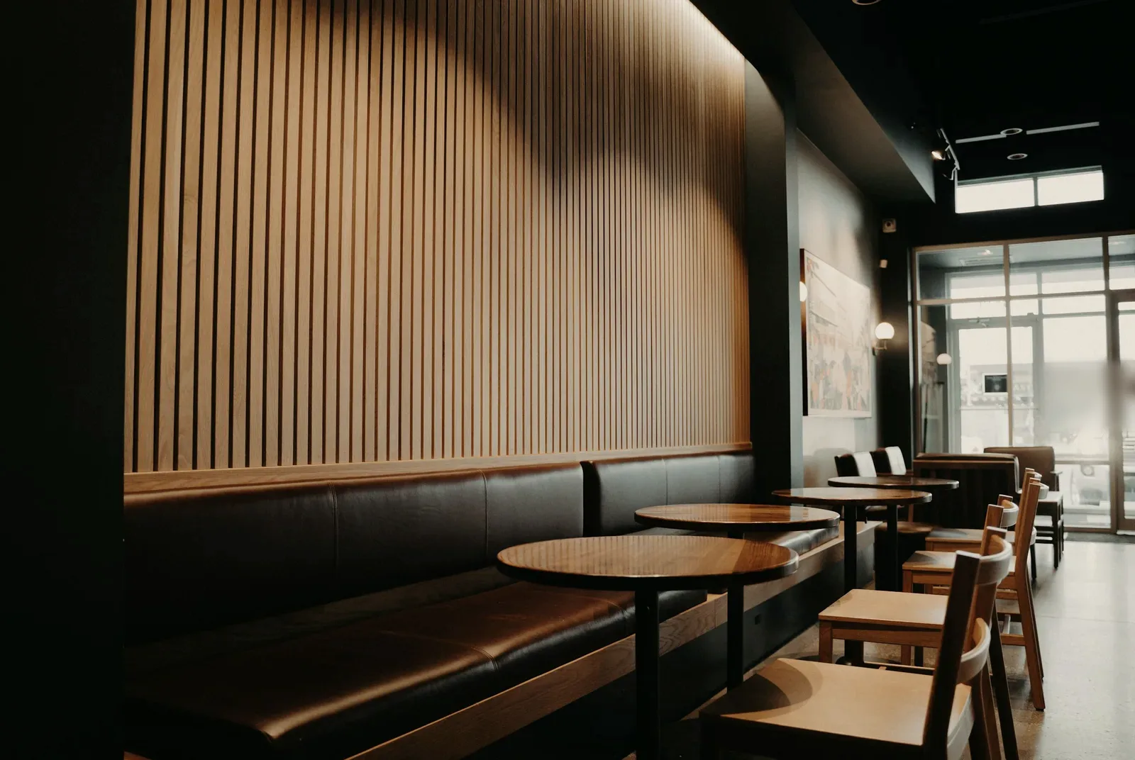 The long bench: a slatted timber wall above a low leather bench, with round tables and loose chairs running towards the daylight at the front.