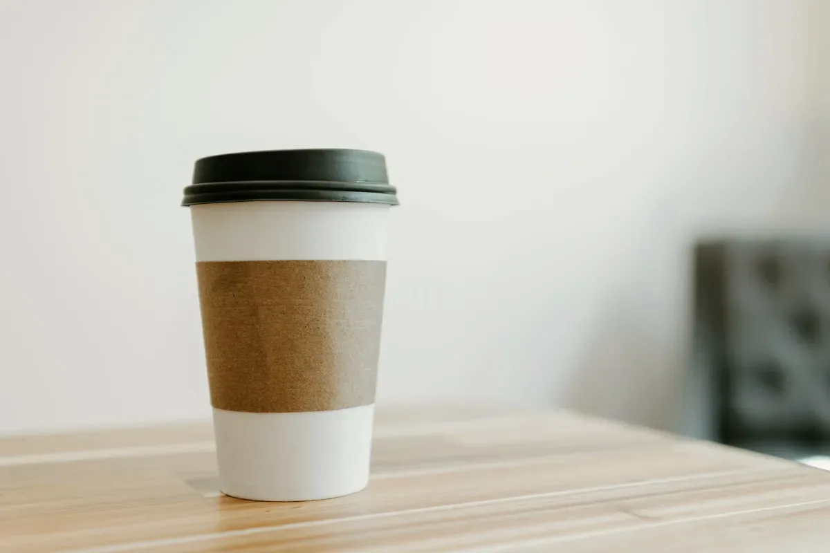 A takeaway cup with a plain kraft sleeve, standing on a pale wooden table.