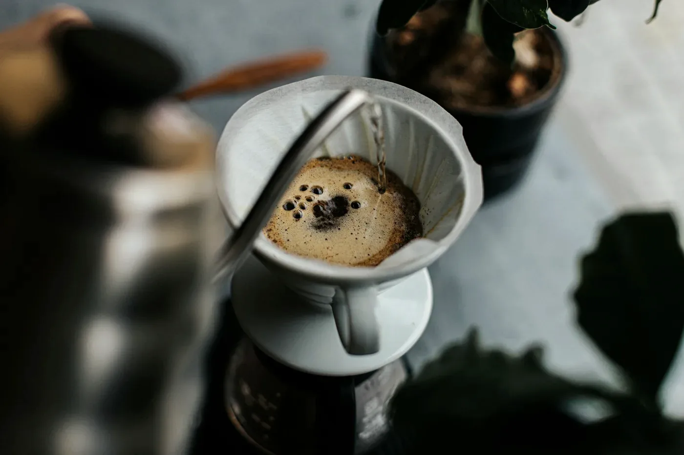 Water poured from a kettle into a white cone dripper, the coffee blooming under it.