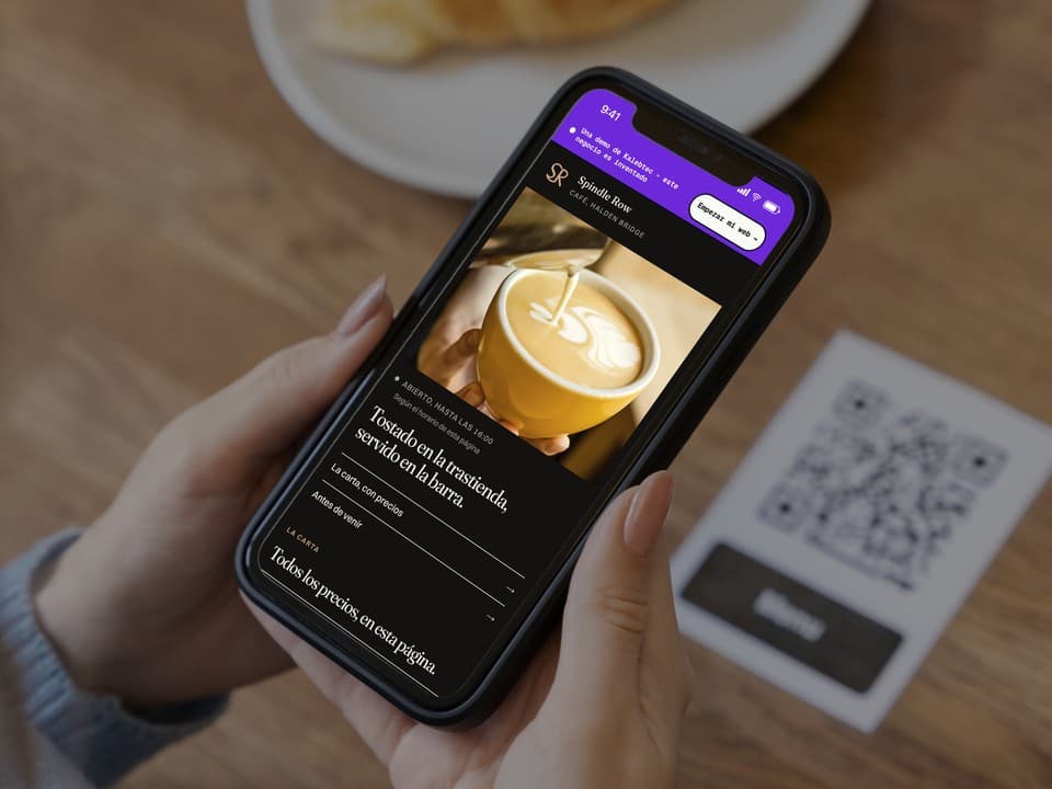 Un móvil abierto en la primera pantalla de la demo de Spindle Row Coffee: una foto de la barra de espresso, el titular «Una sala larga, y nada de música antes de las ocho.» y un enlace a la carta con precios.